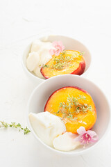Baked peaches served in white plates with mascarpone, pink flower and herbs on the white background. Summer dessert.