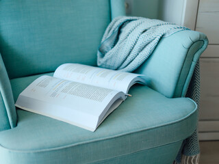 The open book is on a turquoise chair. - Powered by Adobe