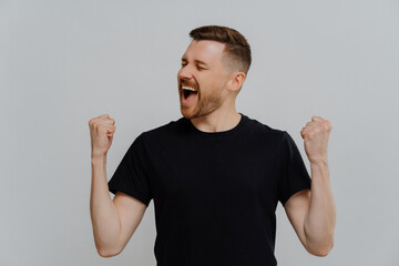 Fototapeta premium Overjoyed emotional happy man raising clenched fists and screaming while celebrating success