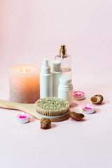 Personal hygiene and body care products, a pink towel and a wooden massage brush lie next to seashells and candles on a pink background.