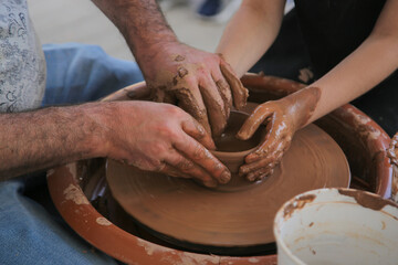  Male's and child's hands  makes a pot on the pottery wheel. Close view the potter's hands make a vase out of fine clay. Creativity․ The idea of ​​traditional crafts.  Handmade pots. 