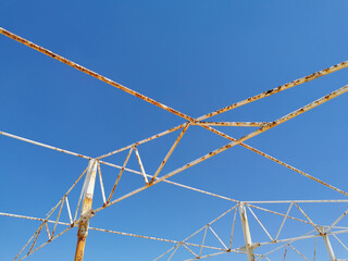 an angular drawing of a structure made of old rusty peeling white pipes and beams against the background of a clear blue sky