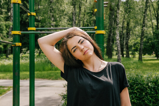 a girl in a black T-shirt is doing neck stretching on the playground