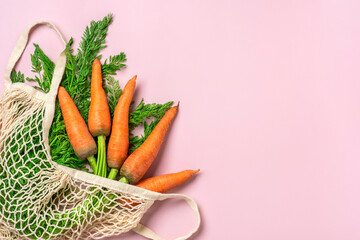 Eco friendly mesh shop bag with fresh harvested carrot isolated on pink background. Flat lay, top view Zero waste, plastic free concept Healthy clean eating diet and detox