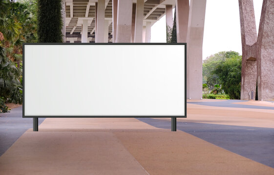 Blank Large Billboard Advertising Banner Mockup In A Large Open Space With Plants Under A Modern Bridge. Large Horizontal Digital Display Screen, An Out-of-home OOH Media Display Space.