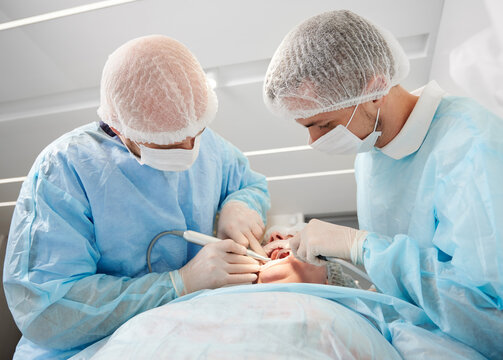 Close-up dental surgery process. Implantation. Dentist surgeon with assistant, wearing disposable clothes, during work using modern technology. Stomatology and health care concept.