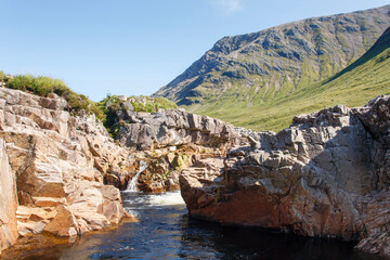 Fototapeta na wymiar Beautiful Glencoe with a stream and blue sky background on a sunny summers day - Scotland