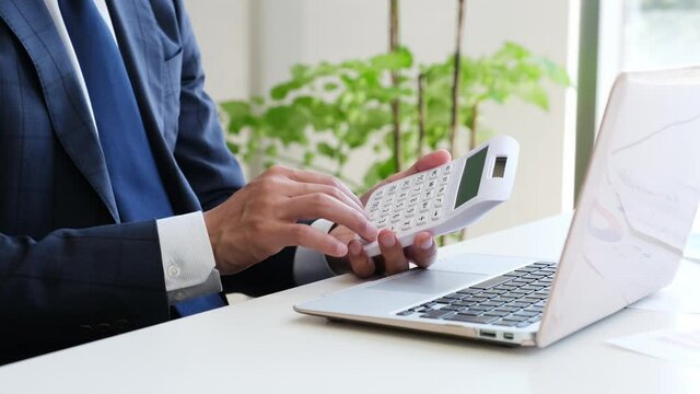 パソコンの前で電卓を操作するサラリーマン男性