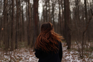 Young woman in autumn forest waving her long hair, dark coat, look from behind, girl in the woods, view on her back