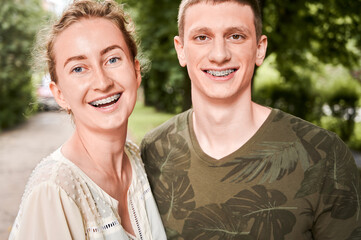 Horizontal snapshot of young couple posing outdoors. Portrait of smiling man and woman in the street wearing dental braces. Orthodontic treatment. Dental care concept