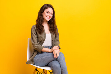 Portrait of attractive confident cheerful girl sitting on chair isolated over vibrant yellow color...