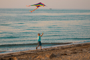 child flies a kite on the beach. A boy runs along the seashore with a bright kite