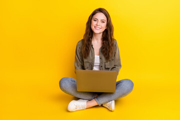Naklejka premium Photo of nice pretty young woman dressed brown shirt sitting floor typing laptop isolated yellow color background