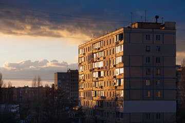 An apartment building in the city is photographed during sunset. There are dark rain clouds in the sky.