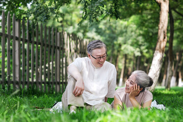 Naklejka na ściany i meble Happy old couple sitting on the park grass watching the scenery