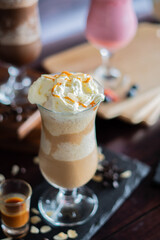 Iced caramel latte coffee frappe in a tall glass with syrup and whipped cream.