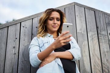 Charming hipster girl browsing social media and networking wireless on modern cellphone gadget, Caucasian female user connecting to 4g internet for writing mail during mobile messaging with followers