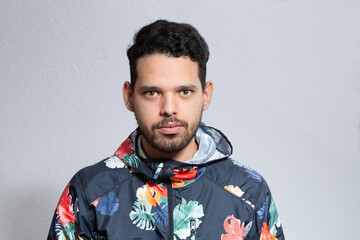 Young latino man frontal portrait in a studio shot. He is serious looking straight to the camera.
