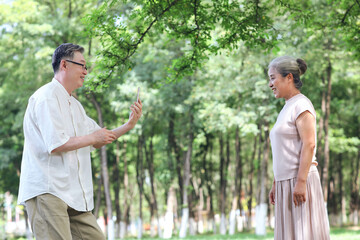 Happy old couple taking photos with mobile phone in the park