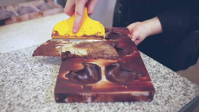 master chef chocolatier rasping away extra dried chocolate from the mold surface. chocolate maker in a professional kitchen.