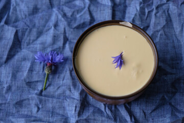 Cornflower petals on home made fresh sour cream. Dairy product on a crumpled canvas. White and blue.