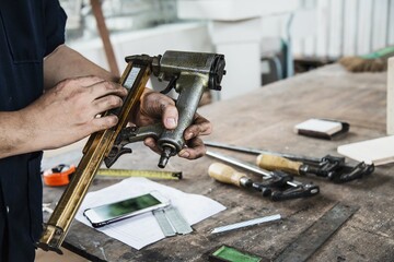 Carpenter using air nail gun doing wooden furniture work