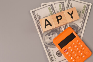 Money banknotes, calculator and wooden blocks written with APY stands for ANNUAL PERCENTAGE YIELD.