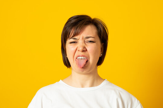 Dissatisfied female frowns face, has disgusting expression, shows tongue, expresses non compliance, irritated with somebody, rejects do something. People and negative facial expressions.