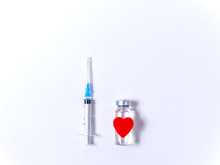 Bottle of the coronavirus vaccine Covid-19 as a gift to a loved one, with a red paper heart and syringe on a white background. Valentine day and Vaccination flu, measles, coronavirus concept. 
