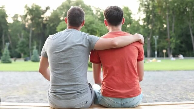 Young gay couple happy sitting on bench in park. Gay couple on romantic date outdoor. gay couple in love flirting. Gay Couple Hugging. Lgbt and love concept. happy men spending time together	