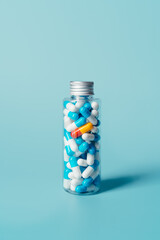 bottle full of white and blue pills or tablets with a single red and yellow pill on a blue background. concept of medicine, pharmacy and coronavirus. vertical image with copy space.