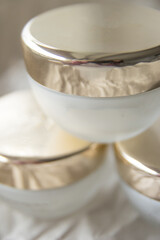 Close up set of a cream jar. Three white glass skincare cosmetic jars with golden lid on ivory background. Three moisturizer. set close up of beauty hygiene container on a background of crumpled paper
