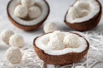 Portions of white chocolate coconut candy balls in the bowl, raw cracked coconut on the background,...