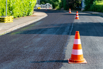 Construction cones marking part of road with a layer of fresh asphalt.