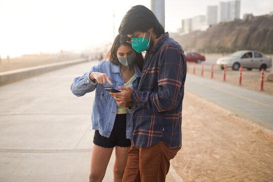 Pareja de j&oacute;venes enamorados revisan sus celulares durante un bello atardecer.