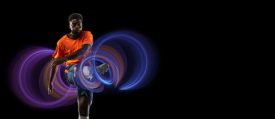 Young african football, soccer player in neon light on black background. Concept of motion and action in sport. Training in jump, flight. Sport, healthy lifestyle, movement, advertising.