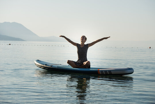 Young woman celebrating life practicing yoga on sup board