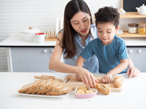 Happy young Asian mother kisses her adorable little son on the cheek while making cookies at home in the kitchen. Funny educational for children concept..