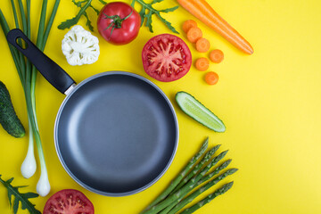 Top view of empty metal frying pan and vegetables on the yellow  background. Copy space. Close-up.