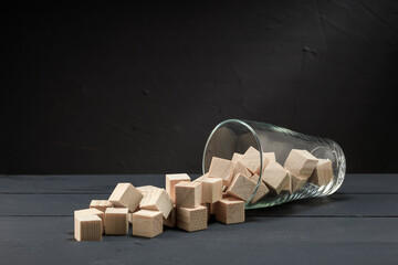 scattered wooden cubes from a glass beaker on a dark surface