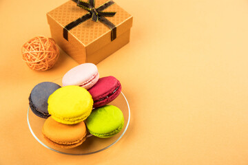 Macaroons cookies on a transparent plate on an orange paper background . Copy space. Sweet gift concept