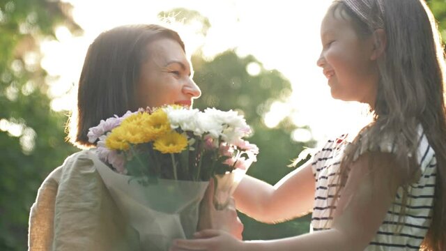 Little girl gives flowers to her mother. Lovely family together. Summer day. Family portrait. Happy motherhood. Enjoy nature. Mothers Day.