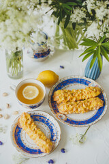 Lemon eclairs and lemon tea, in a vintage tea set, and flowers, over white background.