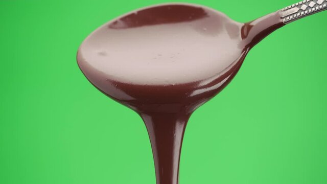 Stream of melted black chocolate pouring from a spoon on a green screen background, chroma key. Template for motion design or advertising.