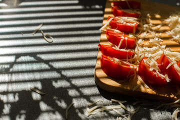 A small pile of grated fresh cheese and red tomatoes lies on a wooden board in the kitchen