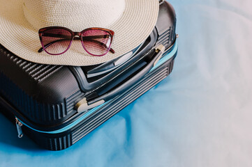 Stylish suitcase with sunglasses and passport on blue background, top view