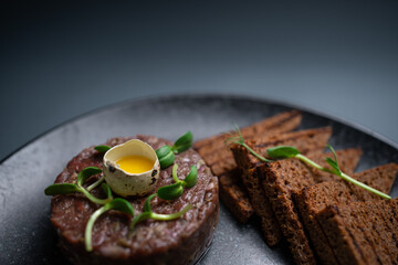 closeup of beef steak tartare with raw egg yolk on plate on black background