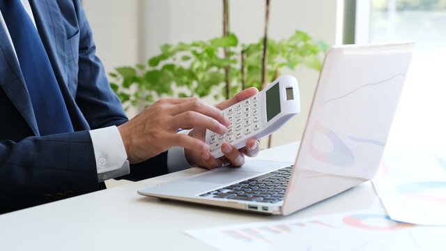 パソコンの前で電卓を操作するサラリーマン男性