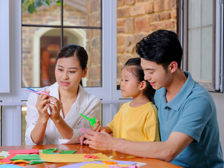 Fototapeta premium A happy family of three doing paper cutting in the living room