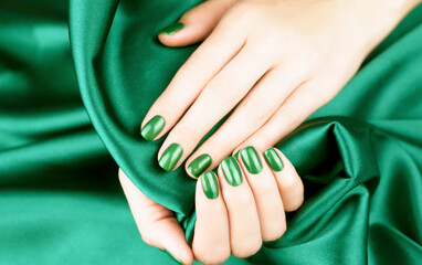 Female hands with bright green manicure on a silk green background